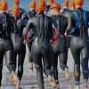Triatleten die in een wetsuit en oranje badmutsen het water in rennen